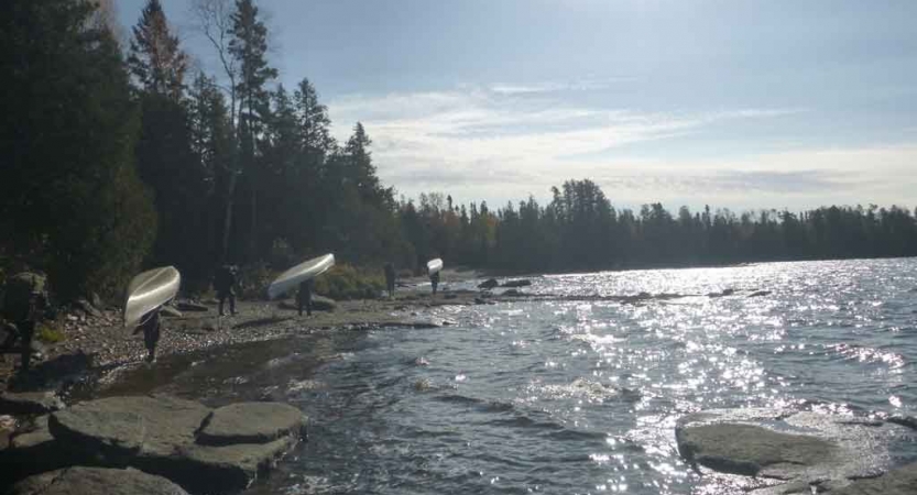 a group of gap year students portage canoes along a lakeshore in Minnesota